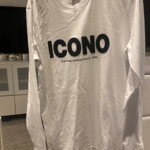 Vit långärmad tröja från ICONO - Snygg vit långärmad tröja från ICONO med stor svart logga på bröstet och texten 'Established since 1999'. Regular fit och tillverkad i mjuk bomull. Perfekt för dig som gillar enkel och clean stil med tydlig branding.