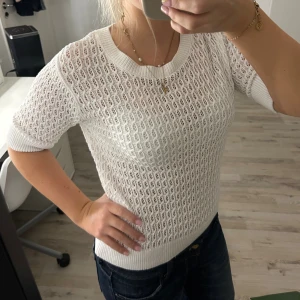 Vit stickad topp från lager 157 - Säljer en vit stickad topp från lager 157 med korta ärmar och rund hals. Tröjan har ett snyggt hålmönster och ribbade muddar vid ärmslut och nederkant. Perfekt för vår och sommar när du vill ha något luftigt men ändå stilrent.