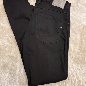 Svarta Replay Anbass  - Svarta jeans från Replay, modell Anbass. Klassisk femficksdesign med Replay-logga på fickan och bakpatch. Jeansen har en slim passform och är tillverkade i mjukt bomullsmaterial med lite stretch för extra komfort. Storlek 32/34