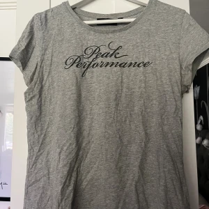 Grå t-shirt från Peak Performance - Snygg grå t-shirt från Peak Performance med svart logga framtill. Klassisk rund halsringning och korta ärmar. Tillverkad i mjuk bomull som känns skön mot huden. Perfekt för en avslappnad och sportig look.