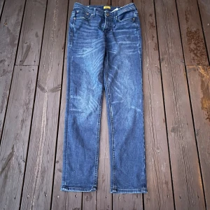 Blå raka jeans i storlek 164 - Snygga blå jeans med klassisk femficksdesign och raka ben. Jeansen har en mörk tvätt med diskreta slitningar framtill och normal passform. Perfekta för dig som gillar en enkel och tidlös look.