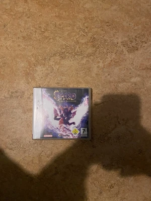 The Legend of Spyro: A New Beginning - Säljer spelet The Legend of Spyro: A New Beginning till Nintendo DS. Omslaget är lila med en bild på draken Spyro och coola blixtar i bakgrunden. Perfekt för dig som gillar action och äventyr med klassiska karaktärer. Spelet är i fysisk kassettform.