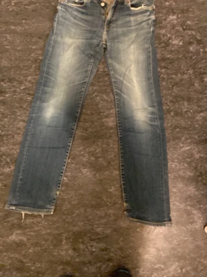 Levi's 501 blå raka jeans - Klassiska blå Levi's 501 jeans med raka ben och slitna detaljer vid benslut. Jeansen har en tidlös passform och är tillverkade i robust denim. Perfekta för dig som gillar en avslappnad och autentisk look.