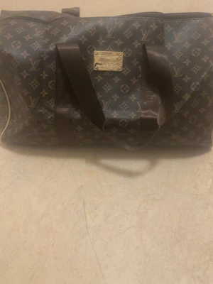 Louis Vuitton monogram resväska - Snygg och klassisk resväska från Louis Vuitton med det ikoniska monogrammönstret i brunt och beige. Väskan har två robusta handtag, guldfärgade metalldetaljer och dragkedja. Perfekt för weekendresor och när du vill resa med stil. Köpt för 12999kr i 2022 men använt fåtal gånger priset kan diskuteras vid slapp affär