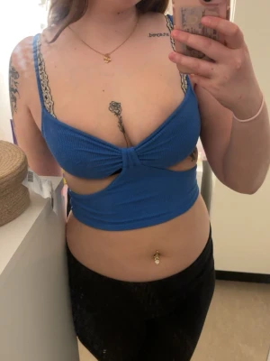 Blå croppad omlottopp - Säljer en blå croppad topp med omlottdetalj. Toppen har en twistad front och öppen rygg med band som går runt midjan.