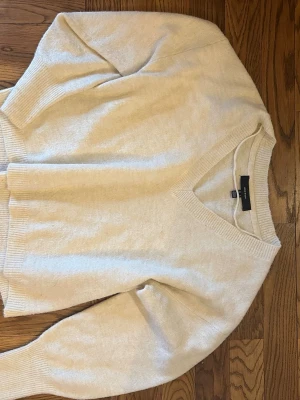 Beige stickad tröja från Vero Moda - Mysig beige stickad tröja från Vero Moda med v-ringning och ribbade muddar vid ärmslut och nederkant. Tröjan har en avslappnad passform och är perfekt för lager på lager. Tillverkad i mjukt material som känns skönt mot huden.