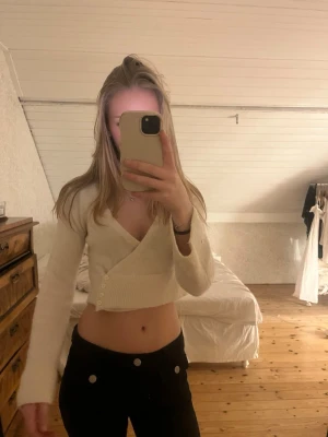 Krämvit omlottkofta med knappar - Trendig krämvit omlottkofta med långa ärmar och snygga knappar på sidan. Kort, croppad modell som passar perfekt till ett linne och ett par snygga byxor. Perfekt för lager-på-lager-stil.