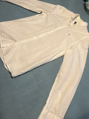 Vit långärmad skjorta från Gant - Klassisk vit skjorta från Gant med lång ärm och knappar framtill. Skjortan har en stilren design med broderad logga på bröstet och är tillverkad i mjuk bomull. Perfekt för en clean och enkel look.