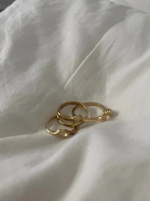 Guldfärgade ringar med hjärtdetalj - Säljer dessa tre guld ringar med olika former, aldrig använda, vet inte vart det är ifrån, köpta för väldigt länge sedan
