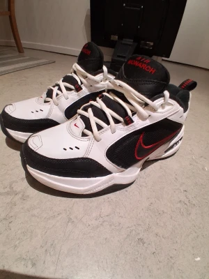 Nike Air max - Nike Air Monarch sneakers i vitt och svart med röda detaljer. Skorna har en klassisk chunky siluett, snörning och rund tå. Ovandelen är i skinn och mesh för bra andningsförmåga. Swoosh-logga i rött på sidan och Air Monarch-tryck på plösen.