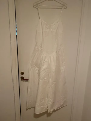 Vit långklänning från Zara - Säljer en vit långklänning från Zara med smala axelband och v-ringad hals. Klänningen har en luftig passform och är tillverkad i bomull, vilket gör den perfekt för varma dagar. Enkel och stilren design som passar till många tillfällen.