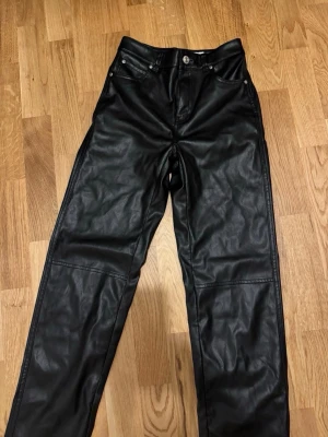 Svarta straight skinnbyxor  - Snygga svarta byxor i skinnimitation med raka ben och klassisk femficksdesign. Byxorna har normal passform och silverfärgade knappar och nitar. Perfekta för en edgy och trendig look.