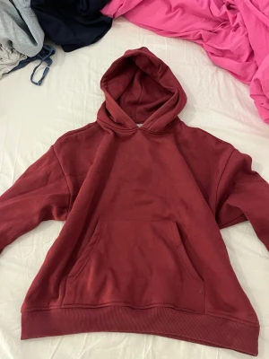 Vinröd hoodie från 157 - Säljer en vinröd hoodie från 157 i storlek M. Hoodien har en klassisk känguruficka framtill och ribbade muddar vid ärmslut och nederkant. Tillverkad i mjukt bomullsmaterial och har en stor huva för extra komfort.