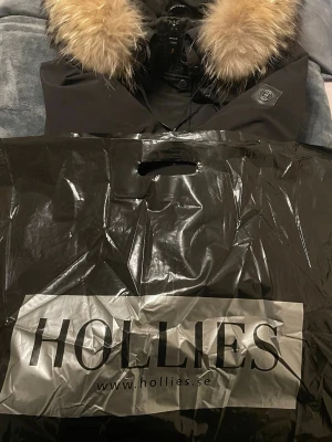 Hollies svart subway jacka med äkta päls  - Säljer min snygga svarta subway dunjacka från Hollies med en lyxig äkta pälsdetalj runt kragen. Perfekt för kalla dagar med sin stilrena design och varma material. Använt i nyskick. Nypris 4000kr Storlek 42 passar både M och L Rökfri jacka. Köpt från Hollies butiken. Finns i Malmö men kan också frakta men köparen står för fraktkostnaden :) vid snabb affär kan jag tänka mig att gå ned i pris 