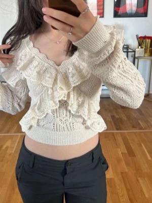 Vit virkad volangtröja - Supersöt vit stickad tröja med virkade detaljer och stora volanger framtill. Tröjan har v-ringning, långa ärmar och ribbad midja. Perfekt för dig som gillar romantisk och trendig stil. Materialet känns mjukt och luftigt.