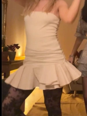 Vit kort klänning med volang - Supersöt vit kort klänning med smala axelband och volangkant nedtill. Klänningen har en figurnära passform och är perfekt för fest. Materialet känns lätt och bekvämt mot huden.