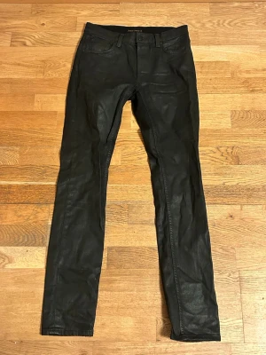 Nudie Jeans Co – Svarta coated jeans – W30 L34 – Mycket bra skick - Snygga svarta skinny jeans från Nudie Jeans med klassisk femficksmodell och smal passform. Jeansen har en lätt glansig finish och är tillverkade i ett stretchigt bomullsmaterial som sitter tajt och bekvämt. Perfekta för dig som gillar en stilren och modern look.