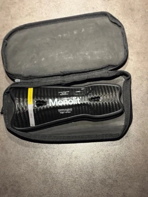 Monolit benskydd i kolfiber med fodral - Säljer ett par svarta benskydd från Monolit i kolfiber med vit logga och text. Kommer i ett svart, vadderat fodral med dragkedja och handtag. Benskydden har en modern, sportig design och är lätta att bära med sig. skriv vid frågor eller kom med bud!