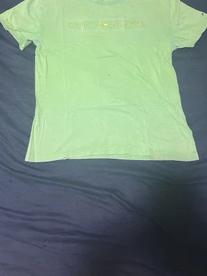 Grön t-shirt från Tommy Hilfiger - Snygg grön t-shirt från Tommy Hilfiger med klassisk logga broderad på bröstet. T-shirten har korta ärmar och rund halsringning. Perfekt för en avslappnad och stilren look.