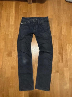 Vintage Diesel Jeans - Säljer ett par mörkblå jeans från Diesel med klassisk femficksdesign och raka ben. Jeansen har tydliga kontrastsömmar och diskret Diesel Industry-logga på myntfickan. Materialet är slitstarkt denim i bomull och passformen är normal/staright. 