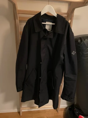J. Lindberg regnjacka - En stilren regnjacka från j.lindberg. Jackan är nästan helt ny med inga defekter och har bara använts sällan. Jackan har snygga designar med ett bra knappsystem. Perfekt för dig som vill se stilig och hålla sig varm under vintern och våren.