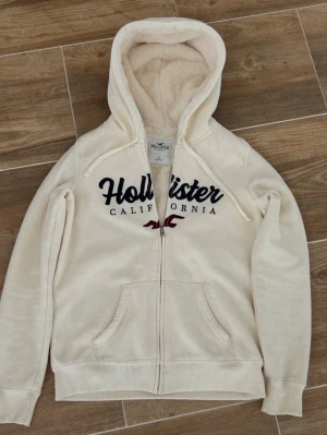Vit/ beige Hollister hoodie/med dragkedja - bra skick - Vit/ beige hoodie från Hollister i jättefint skick. Mjuk och skön med snygg passform, perfekt till vardags och chill outfits. Inga fläckar eller hål. Kommer inte till användning längre 🤍