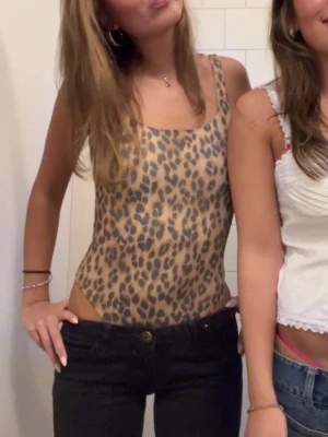 Leopardmönstrad body med breda axelband - Snygg body med leopardmönster i beige och bruna toner. Modellen har breda axelband och fyrkantig ringning. Stretchigt material som sitter tight och bekvämt. Perfekt för dig som vill sticka ut med ett djurmönstrat plagg.