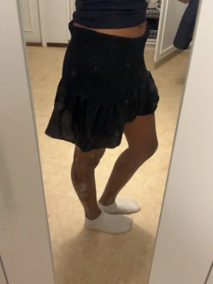 Svart volangkjol med resårmidja - Supersöt svart kortkjol med volangkant och bred resår i midjan. Kjolen har en luftig och flowy känsla som passar perfekt till både sneakers och boots. Enkel att matcha med olika toppar för en trendig look.