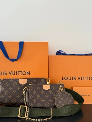 Louis Vuitton Multi Pochette Accessoires - Säljer en Louis Vuitton Multi Pochette Accessoires i klassiskt brunt monogramcanvas med guldiga detaljer. Väskan har flera delar: två necessärer och en rund myntplånbok, samt en bred grön axelrem och en guldfärgad kedja. Perfekt för dig som gillar trendiga och lyxiga accessoarer. Ordinarie pris 26,600:- Kvitto, dustbag, kartong och påse finns med! 
