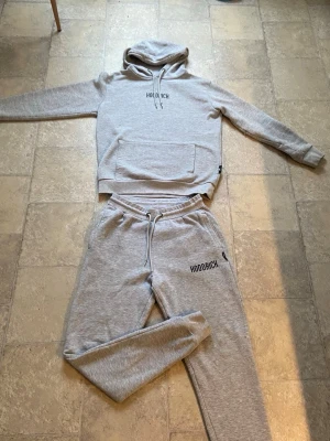 Grått Hoodrich mjukis set - Mysigt grått loungewear set från Hoodrich med matchande hoodie och byxor. Hoodien har magficka och dragsko i huvan, medan byxorna har resår i midjan och dragsko samt fickor. Båda delarna har Hoodrich-logga tryckt framtill. 