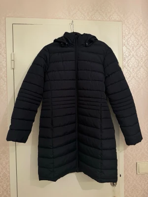 Svart lång pufferjacka med huva - Dessa jackor från Tuxer säljs för 700kr. Knappt använd. En svart lång pufferjacka med huva och dragkedja framtill. Jackan har horisontella quiltade sömmar, två sidofickor med dragkedja och en skön, rymlig passform. Perfekt för kalla dagar när du vill hålla dig varm och stilsäker. Storlek M. 