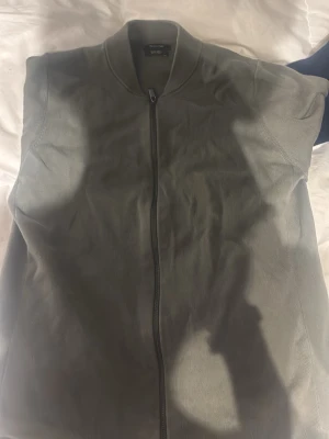 Grå grön zip från Massimo Dutti - Säljer en stilren grå grön zip från Massimo Dutti. Jackan har ribbad krage och muddar, hel dragkedja framtill och är gjord i mjuk bomull. Perfekt för dig som gillar en clean och enkel look.