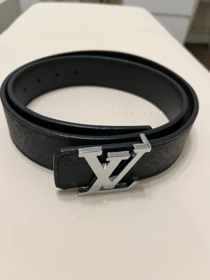 svart läderbälte - Snyggt svart bälte i äkta läder med klassiskt spänne i silverfärgad metall. Bältet har diskret monogrammönster längs remmen och justerbara hål för perfekt passform. Perfekt accessoar för att lyfta din outfit.