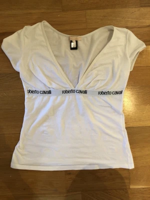 Vit v-ringad topp Roberto Cavalli - Säljer en vit topp från Roberto Cavalli med djup v-ringning och korta ärmar. Storlek 40 IT, Det passar som XXS!