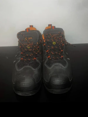 Svarta arbetsskor från Gesto med orange detaljer - Säljer ett par svarta arbetsskor från Gesto med orange insida och detaljer samt reflexinslag på sidorna.