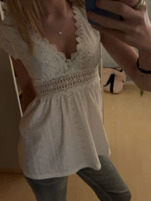 Vit spetsblus med broderade detaljer - Supersöt vit blus med broderade hålmönster och bred spets i midjan. V-ringad med spetskant och korta ärmar. Luftig och flowy passform, perfekt till sommaren. Tillverkad i bomull och har romantiska detaljer som gör den extra speciell. Passar S också💓💓