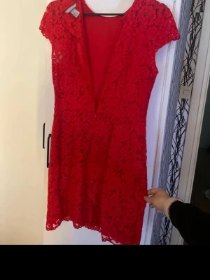 Röd spetsklänning från H&M - Säljer en röd kortklänning från H&M i storlek 38. Klänningen har v-ringning, korta ärmar och är täckt av ett blommigt spetsmönster. Dragkedja i sidan för enkel påklädning. Perfekt för dig som vill sticka ut med en färgstark look!