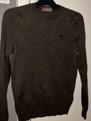 Mörkbrun merinoullströja Morris S - Säljer en mörkbrun, klassisk rundhalsad tröja från Morris i 100% merinoull. Tröjan har diskret broderad logga på bröstet och ribbade muddar vid ärmslut och nederkant. Perfekt för dig som gillar stilrena och tidlösa plagg.