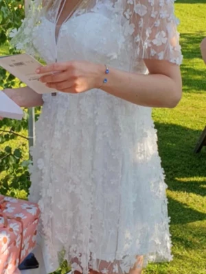 Vit studentklänning med blommor från Bubbleroom - Supersöt vit studentklänning från Bubbleroom med 3D-blommor och transparent mesh upptill. Använd en gång