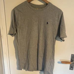 Grå t-shirt från Ralph Lauren - Klassisk grå t-shirt från Ralph Lauren med liten broderad logga på bröstet. T-shirten har rund halsringning och är tillverkad i mjuk bomull. Perfekt basic-plagg till garderoben.