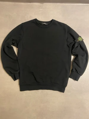 Svart sweatshirt från Stone Island - Säljer en svart sweatshirt från Stone Island i storlek M. Tröjan har klassisk rund hals, ribbade muddar och den ikoniska Stone Island-patchen på vänster ärm. Tillverkad i mjuk bomull för skön passform och stilren look.