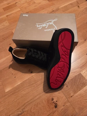 Christian Louboutin Louis Strass sneakers - Säljer ett par svarta Christian Louboutin Louis Strass sneakers i mocka med ikonisk röd sula och svarta nitar på tån. Skorna har snörning och en lyxig känsla med beige skinnfoder. Perfekt för dig som vill sticka ut med exklusiva detaljer. Kommer med orginalkvitto i kronor som valuta, inte något skumkvitto från Hong Kong som fakes har. Nypris står på kvittot, 10 009 kr.