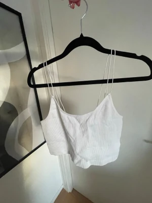 Vit ribbad croppad linnetopp - En vit croppad linnetopp med tunna dubbla axelband och ribbad struktur. Från Gina Tricot 