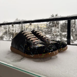 Svarta Maison Margiela Gats  - Ett par riktigt feta Maison Margiela gats i svart skinn med paint splatter. Beige snörning och brun gummisula ger en clean kontrast. Storlek 44, sitter TTS enligt mig. Priset är såklart diskuterbart vid snabb affär, hör av er vid frågor!