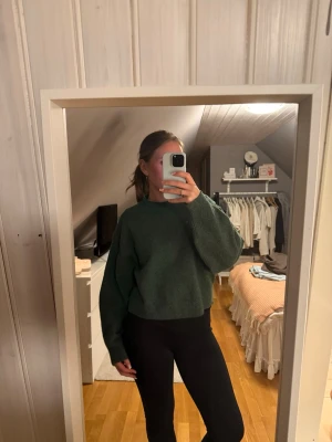Grön stickad tröja med loose fit - Mysig grön stickad tröja med rund hals och avslappnad, lite oversized passform. Tröjan har långa ärmar och ribbade muddar vid ärmslut och nederkant. .