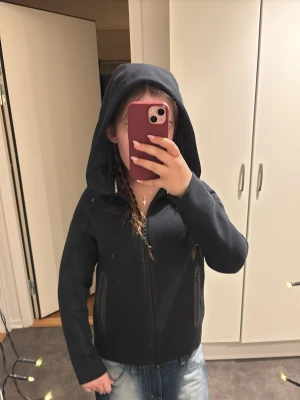 Svart Nike tech hoodie med dragkedja strl 147 (M) - Säljer en svart hoodie från Nike (barnmodell) strl M/147. Tröjan har hel dragkedja framtill, två fickor med dragkedja och en stor huva. Materialet känns mjukt och sportig. Nike-logga på bröstet.