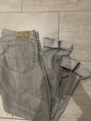 Grå 🔥(selvedge denim)🔥 jeans  från Polo Ralph Lauren - Säljer ett par grå jeans från Polo Ralph Lauren med klassisk femficksdesign och diskret RL-broderi vid fickan. Jeansen har raka ben och är tillverkade i mjukt bomullsmaterial. Snygg  tvättad look och detaljerade sömmar. Jeans är uppsydda och passar någon som bär 33/32 bättre 