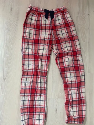 Rödvitrutiga mjukisbyxor - Säljer ett par mjuka och sköna byxor med rödvitt rutigt mönster och blå snörning i midjan. Perfekta för hemma dagar eller chillkvällar. Tillverkade i bomull för extra komfort. Säljer då dom blivit förkorta. Storlek 146/152