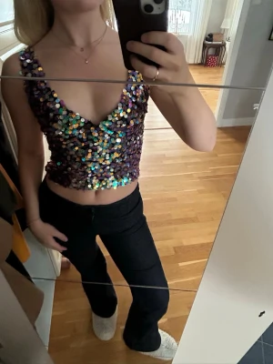 Glittrig paljettopp med djup v-ringning - Säljer en croppad topp täckt av glittriga paljetter i lila och silvertoner. Toppen har en djup v-ringning och är ärmlös med breda axelband. Perfekt för dig som vill sticka ut på festen!