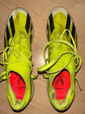 Adidas Crazyfast gula fotbollsskor - Säljer ett par Adidas Crazyfast fotbollsskor i neon-gult med svarta och blå detaljer. Skorna har snörning, spetsig tå och metall-dobbar för bästa grepp på planen. Ovandelen är i lätt syntetmaterial och innersulan är röd med Crazyfast-tryck. Nypris 2999